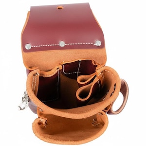 May include: Open view of a burgundy leather tool pouch with multiple compartments. The pouch has a flap closure secured with silver rivets and a metal clasp. The interior is a darker burgundy color, and the edges are stitched with white thread. A small handle is visible.