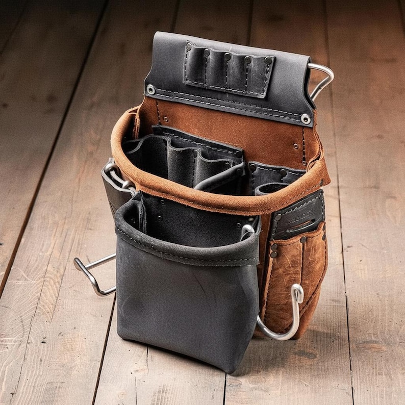 May include: A leather tool pouch featuring a combination of brown and black leather sections. The pouch includes multiple open compartments, several smaller slots for tools, a metal hammer loop, and a metal hook attached to the side for storage.