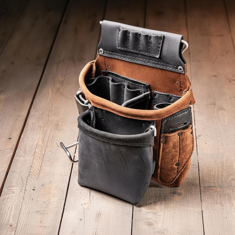 May include: A tool pouch constructed from brown and black leather, featuring multiple open compartments, a front pocket, and a top section with four small slots for tools. The pouch is secured with metal rivets and includes a metal loop on the side.
