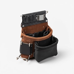 May include: A brown and black leather tool belt with multiple pockets and a metal clip. The tool belt has a suede-like texture and is designed to be worn around the waist. It features a variety of compartments for tools.
