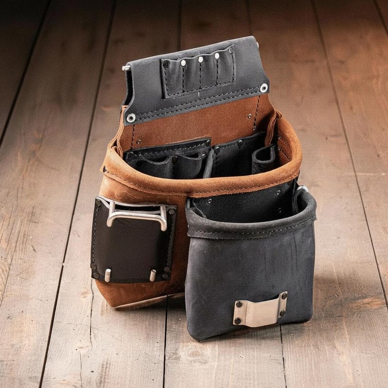 May include: A brown and black leather tool pouch featuring multiple open compartments, a metal hammer loop, and a metal tape measure clip. The construction includes reinforced rivets and stitched seams, providing several pockets for organizing various hand tools.