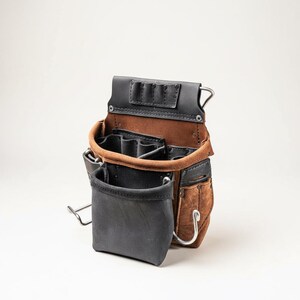 May include: A brown and black leather tool pouch featuring multiple compartments, a large front pocket, and integrated metal loops. The construction includes reinforced stitching, metal rivets, and a dedicated top section with three small slots for tools.