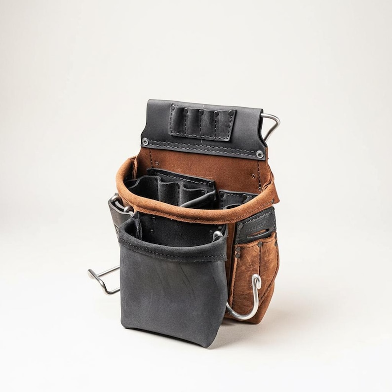 May include: A brown and black leather tool pouch featuring multiple compartments, a large front pocket, and integrated metal loops. The construction includes reinforced stitching, metal rivets, and a dedicated top section with three small slots for tools.
