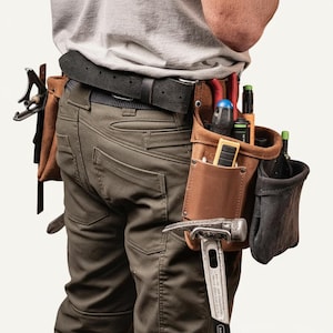 May include: A brown leather tool belt with multiple pockets and loops, holding various tools including a hammer, screwdrivers, and pliers. The belt is worn around the waist over green work pants and a black belt.