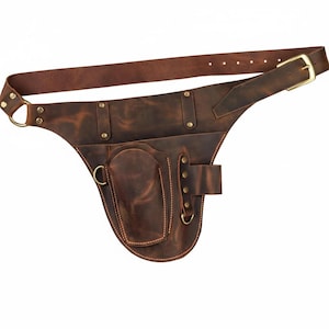 Op de afbeelding: Een bruine leren heuptas met meerdere vakken en een riem. De tas heeft een hoofdvak, een kleiner vak en een riemlus met een messing gesp. Het leer heeft een distressed look.