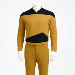 May include: Mustard yellow Star Trek uniform with black detailing. The long-sleeved top has a black shoulder yoke and a black geometric design. The matching trousers have a straight leg design. The uniform is displayed on a mannequin.