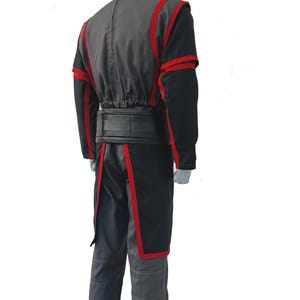 K&ouml;nnte beinhalten: Ein Kost&uuml;m bestehend aus einer anthrazitfarbenen und schwarzen Jacke mit rotem Besatz, langen &Auml;rmeln und einem Stehkragen. Das Outfit umfasst einen breiten schwarzen G&uuml;rtel und eine passende anthrazitfarbene Hose mit sichtbaren N&auml;hten sowie eine Tunika.
