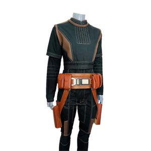 K&ouml;nnte beinhalten: Schwarzes und braunes Cosplay-Kost&uuml;m mit hohem Kragen und langen &Auml;rmeln. Das Kost&uuml;m hat braune Akzente an Schultern und Brust, einen braunen G&uuml;rtel mit Taschen und holsterartige Beinbefestigungen. Das Outfit ist mit vertikalen N&auml;hten versehen.