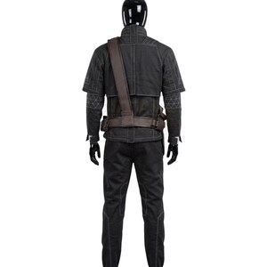 May include: A black long-sleeved jacket and matching trousers set featuring white contrast stitching and geometric patterns on the sleeves. The outfit includes a brown utility belt with a shoulder strap worn over the jacket, displayed on a mannequin.