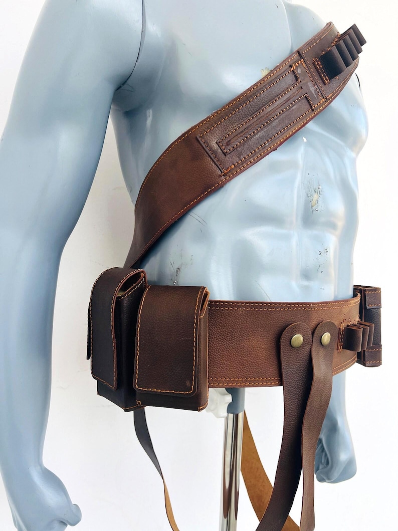 May include: A brown leather bandolier and utility belt set featuring multiple pouches, loops for small cylindrical items, and brass-colored metal snap fasteners. The gear is worn across the torso and around the waist, constructed with visible stitching along the edges of the leather components.