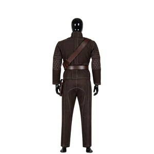 May include: A brown costume displayed on a black mannequin. The outfit includes a jacket, pants, belt, and shoulder strap. The jacket has a high collar and geometric stitching on the shoulders. The pants have white stitching.