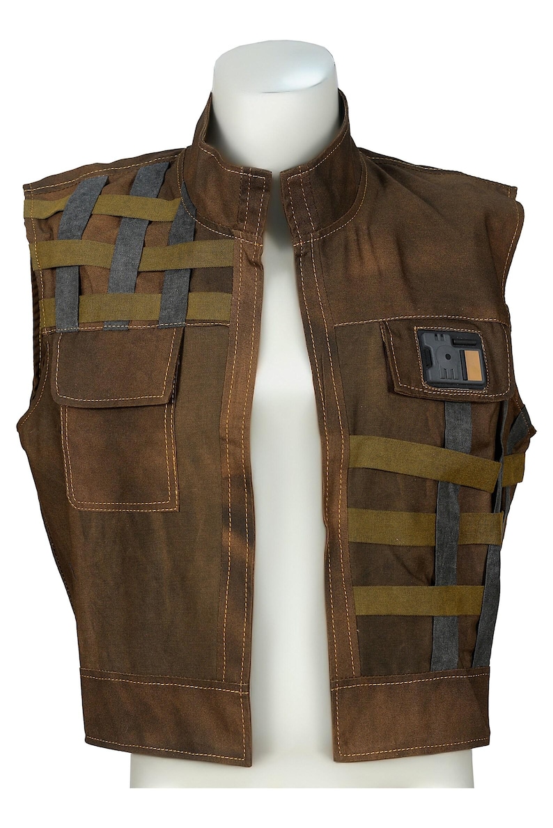 May include: A brown sleeveless vest featuring a high collar, visible stitching, and a woven strap pattern in olive green and dark gray. The garment includes two front pockets, one of which is adorned with a rectangular black and tan badge.