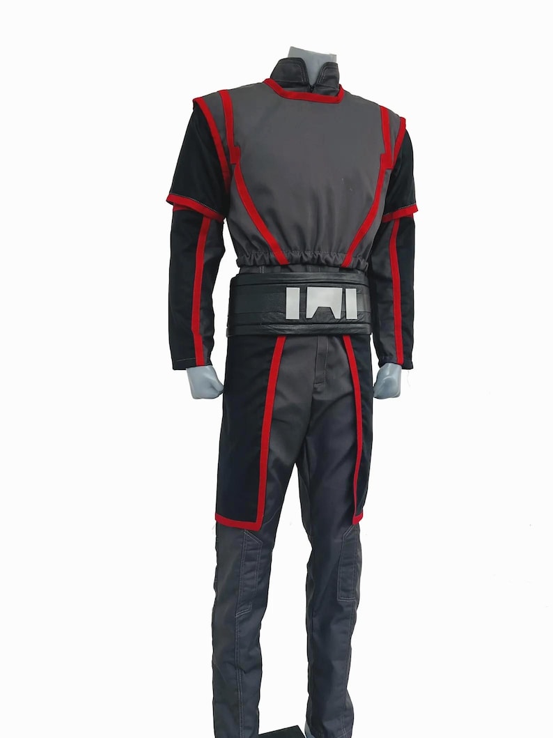 K&ouml;nnte beinhalten: Ein lang&auml;rmeliges Tunika- und Hosenset in Grau und Schwarz mit roten Zierstreifen an Schultern, Brust und Beinen. Das Outfit enth&auml;lt einen breiten schwarzen G&uuml;rtel mit einer silbernen, rechteckigen Schnalle im Taillenbereich.
