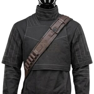 May include: A black high-collared tunic with white stitching details worn with a brown cross-body bandolier. The bandolier features a series of small cylindrical loops for storage, adjustable metal buckles, and a structured strap design across the chest.