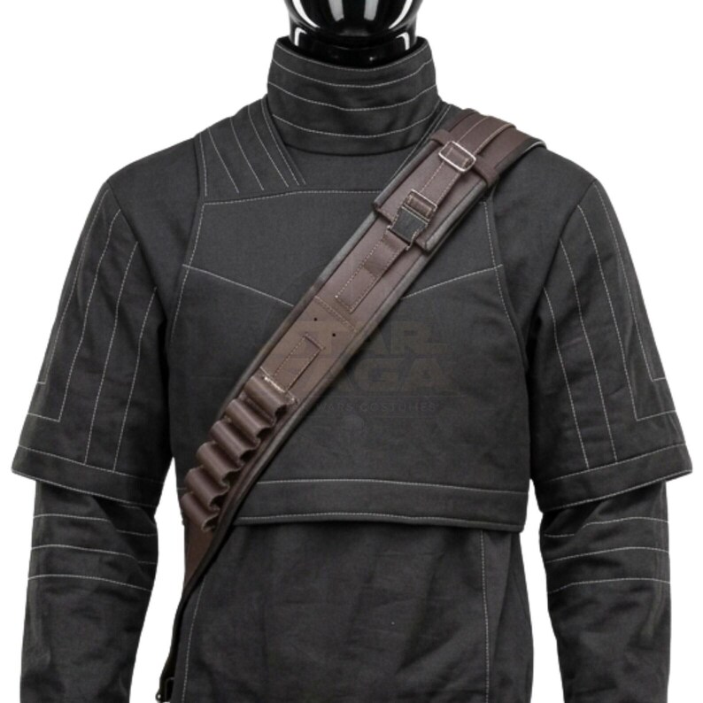 May include: A black high-collared tunic with white stitching details worn with a brown cross-body bandolier. The bandolier features a series of small cylindrical loops for storage, adjustable metal buckles, and a structured strap design across the chest.