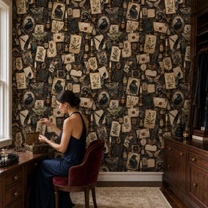 Op de afbeelding: Behang met een donker, complex patroon van zwarte raven, vintage brieven, botanische illustraties, motten en apothekersflessen. Het ontwerp bevat goudkleurige accenten en kandelaars tegen een diepe, donkere achtergrond.