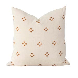 May include: Cream-colored decorative pillow with a repeating pattern of small, brown cross-like shapes. The pillow has a soft, textured appearance and is square-shaped, perfect for adding a touch of style to any living space.