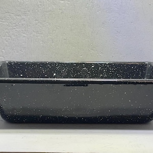 Puede incluir: Una bandeja rectangular para hornear de esmalte negro con motas blancas. La bandeja tiene un borde ligeramente elevado y está sobre una superficie blanca. Esta bandeja de estilo vintage es adecuada para hornear.