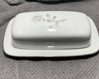 Könnte beinhalten: Weißes Porzellan-Buttergericht mit rechteckigem Deckel und Boden. Der Deckel zeigt ein zartes graues Rosen- und Stieldesign. Der Boden hat eine silberne Zierleiste. Für einen Standard-Butterblock konzipiert.