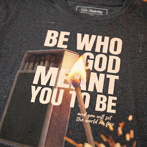 May include: Charcoal grey t-shirt with the text "BE WHO GOD MEANT YOU TO BE" and "and you will set the world on fire." The design includes a lit match and a matchbox.