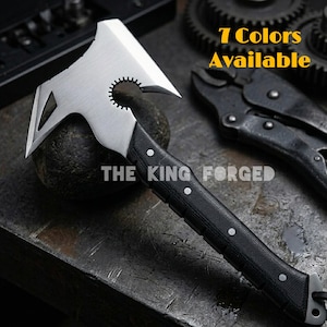 Pode incluir: Um machado tático prateado e preto com um cabo preto texturizado e rebites brancos. A cabeça do machado tem um design único com uma aresta de corte, um pico e uma função de chave. O texto "THE KING FORGED" é visível. O texto "7 Colors Available" também é visível.