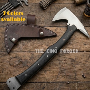Könnte beinhalten: Eine geschmiedete Stahlaxt mit schwarzem Griff und brauner Lederscheide. Die Axt hat eine silberne Klinge und der Text "THE KING FORGED" ist sichtbar. Das Bild enthält auch den Text "7 Colors Available".