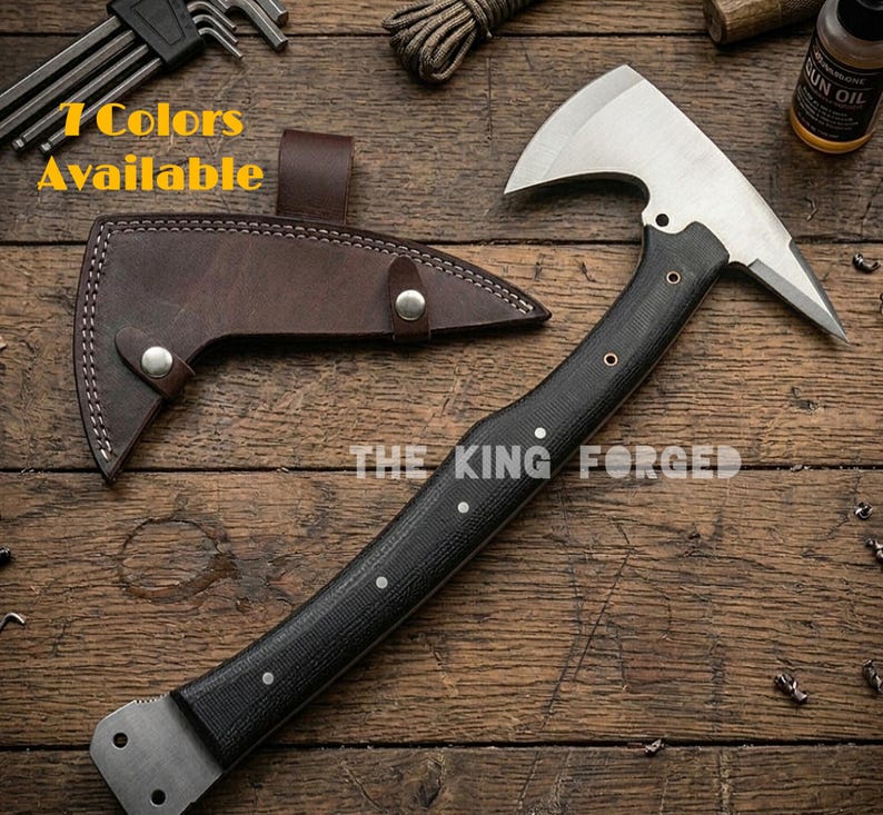 Puede incluir: Un hacha de acero forjado con mango negro y funda de cuero marr&oacute;n. El hacha tiene una hoja plateada y el texto "THE KING FORGED" es visible. La imagen tambi&eacute;n incluye el texto "7 Colors Available".