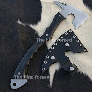 Pode incluir: Um machado preto e prateado com um cabo curvo e uma cabeça estilo tomahawk. O machado tem um cabo preto e uma lâmina prateada. Uma bainha de couro preta está incluída. O texto "The King Forged" é visível.