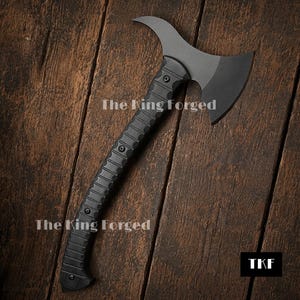 May include: A matte black double-bit axe featuring a curved handle with a textured grip and visible screw fasteners. The blade head has a distinct crescent shape. The text The King Forged is visible on the blade, and the letters TKF appear in a black square in the corner.
