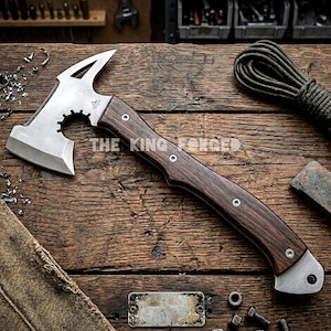Pode incluir: Um machado artesanal com uma lâmina de aço inoxidável e um cabo de madeira escura. A cabeça do machado apresenta um design único com uma borda dentada e um topo pontiagudo. O cabo é fixado com rebites de metal. O texto "THE KING FORGED" é visível.