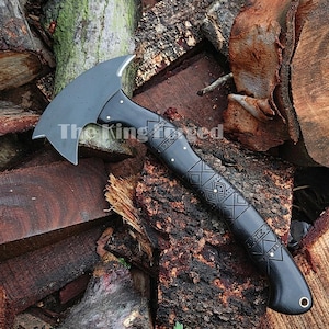 May include: A black axe with a curved blade and a patterned handle. The handle features geometric designs and the text "The King's Creed". The axe is resting on a pile of wood.