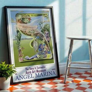 May include: Framed art print titled "Angel Marina" featuring a surrealist illustration with a woman's profile, flowers, and a clock. The artwork is in a black frame, leaning against a blue wall. A small white stool and potted plant are nearby.