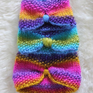 Può includere: Un set di tre berretti di lana colorati con un motivo arcobaleno. I berretti sono realizzati con un filato morbido e hanno una texture soffice.