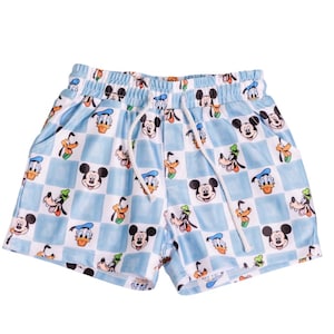 Puede incluir: Shorts de color azul claro con un estampado de cuadros blancos con Mickey Mouse, Donald Duck y Goofy. Los shorts tienen cintura con cordón y bolsillos. Los shorts están hechos de una tela suave y ligera.
