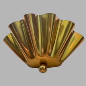 Op de afbeelding: Een kom van gepolijst messing in de vorm van een waaier of een schelp met diepe verticale ribbels. De kom heeft een glad, reflecterend metalen oppervlak en rust op een kleine, ronde messing bolvormige voet aan de onderzijde.