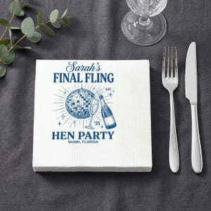 May include: White square napkins with a blue design. The text reads "Sarah's Final Fling Hen Party Miami, Florida". The design includes a disco ball, champagne bottle, and glass. A fork, knife, and glass are on a grey surface.