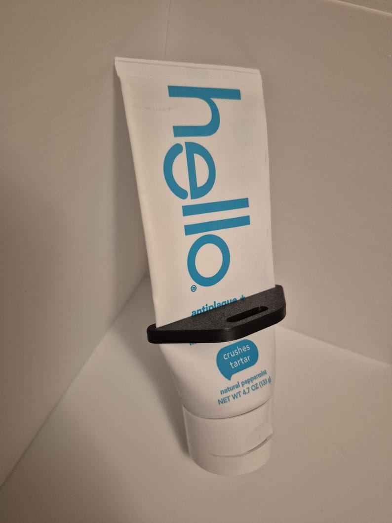 Pode incluir: Um tubo branco de pasta de dentes "hello" de hortel&atilde;-pimenta natural, preso em um suporte preto. O tubo tem texto azul e uma bolha azul que diz "crushes tartar". Peso l&iacute;quido 133g.