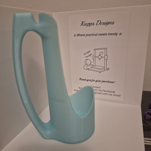 May include: A light blue, 3D-printed kitchen utensil holder with a curved handle and a cradle-like base. The holder is displayed with a card that reads "Krepps Designs" and "Where practical meets trendy."