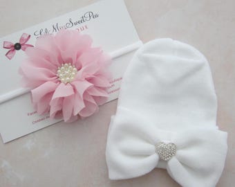 May include: A white baby hat with a large bow and a rhinestone heart-shaped embellishment. A pink chiffon flower headband with a pearl center is also present. The text "Lila Miss Sweet Pea" is visible on a card.