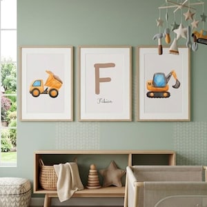 Könnte beinhalten: Drei gerahmte Aquarelldrucke mit Baumaschinen: ein Muldenkipper, der Buchstabe "F" mit dem Namen "Fabian" und ein Bagger. Die Drucke befinden sich in einem Kinderzimmer mit einem Holzbett, einem Teppich und einem Mobile.