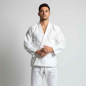May include: A white martial arts uniform, comprising a jacket and trousers. The jacket has a V-neck design and the brand name "RVCA" is visible. The trousers have a drawstring waist and a logo. The uniform is made of a robust fabric.