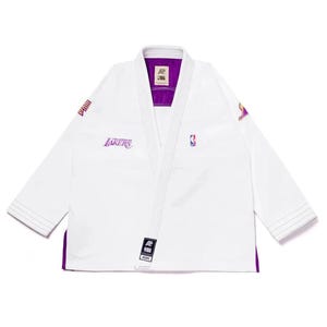 May include: White martial arts uniform with purple trim and accents. Features the Los Angeles Lakers team logo and NBA logo. Includes the brand's logo and text. A sports-themed gi.
