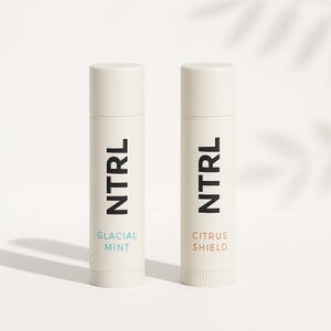 May include: Two white lip balm tubes with black "NTRL" text. One tube has "GLACIAL MINT" in light blue, the other has "CITRUS SHIELD" in light brown. The tubes have a ribbed base and a white cap.