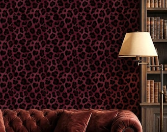 Op de afbeelding: Een dieprode gecapitonneerde fluwelen bank staat tegen een muur met een donkerbordeaux en zwart luipaardpatroon. Naast de bank staat een hoge houten boekenkast gevuld met boeken, een vloerlamp, een wereldbol op een standaard en een koperen kandelaar.