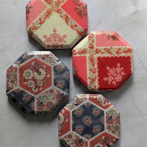 Puede incluir: Cuatro posavasos octogonales con variados patrones florales y geométricos en tonos rojo, crema y azul marino. Cada posavasos tiene un acabado brillante con diseños impresos intrincados, incluyendo pequeños racimos de flores y bordes.