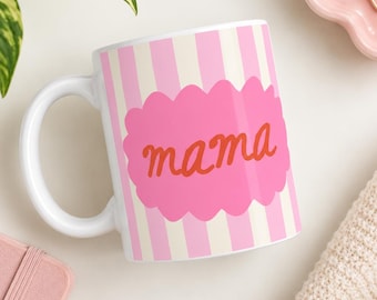 May include: A white ceramic mug featuring vertical light pink and cream stripes. In the center, a bright pink scalloped-edge oval shape contains the word mama written in a cursive, reddish-orange font across the front of the mug.