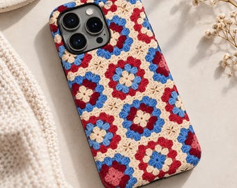 May include: A smartphone case featuring a repeating granny square crochet pattern in cream, light blue, and deep red. The design covers the back of the device, including the area around the triple-lens camera module, with a textured, yarn-like appearance.