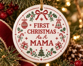 May include: A round white ceramic Christmas ornament featuring a red and green cross-stitch pattern. The text reads First Christmas As A Mama, surrounded by illustrations of a bow, bell, candy canes, gifts, and a tree with holly leaves.