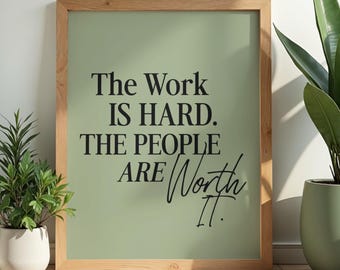 Puede incluir: Un cuadro enmarcado con el texto "The Work IS HARD. THE PEOPLE ARE Worth It." El fondo es verde apagado y el texto es negro. El marco es de madera clara. Hay plantas en macetas a ambos lados.
