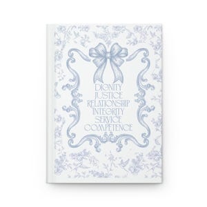 Puede incluir: Un diario blanco con un estampado floral azul y un marco decorativo. El marco contiene las palabras "DIGNIDAD, JUSTICIA, RELACIÓN, INTEGRIDAD, SERVICIO, COMPETENCIA". Un lazo azul adorna la parte superior del marco.